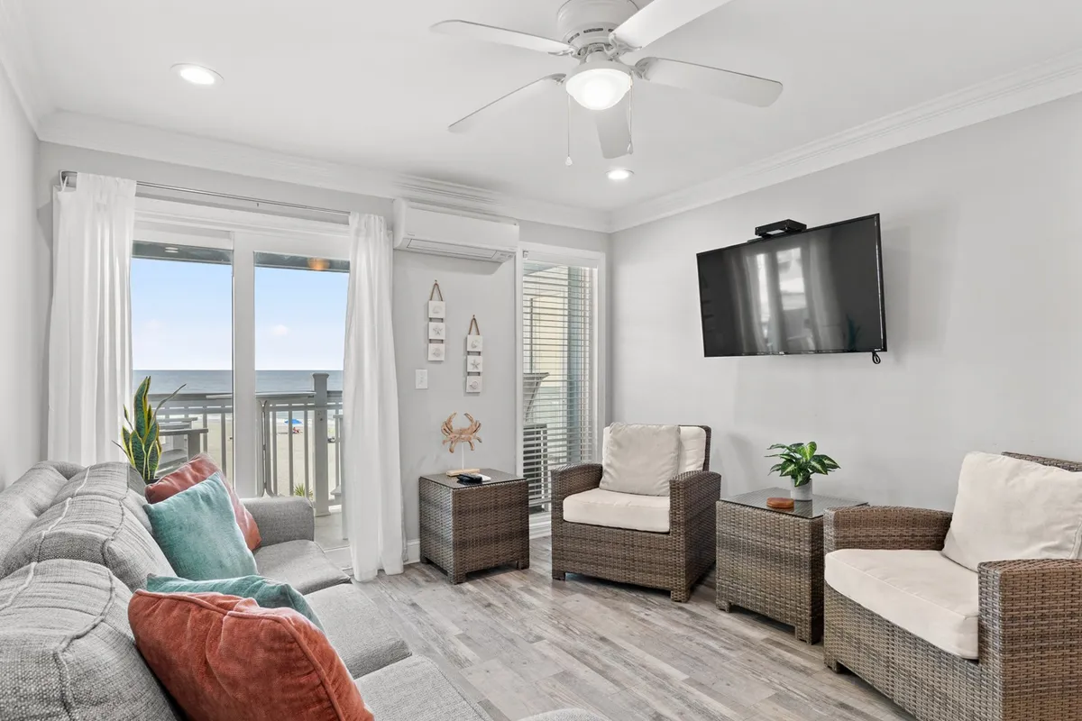 A bright and welcoming living area featuring a comfortable sofa with colorful cushions positioned to enjoy both the flat-screen TV and stunning ocean views through expansive windows. A plant on the table adds a touch of nature, and the overall ambiance is cozy and inviting.