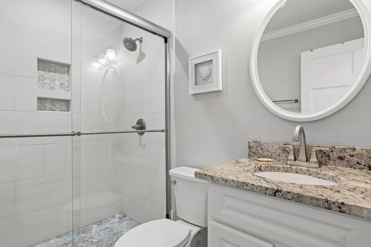 A modern bathroom with a glass shower enclosure, granite countertop, and a round mirror. The space is bright, tidy, and inviting—perfect for refreshing after a day outdoors.