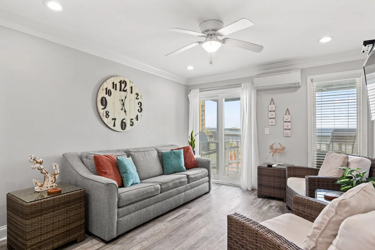 A casual and comfortable living space with a large wall clock, sofa adorned with accent pillows, and doors leading out to a private balcony. The scene invites moments of relaxation, with the balcony promising fresh air and beautiful vistas.