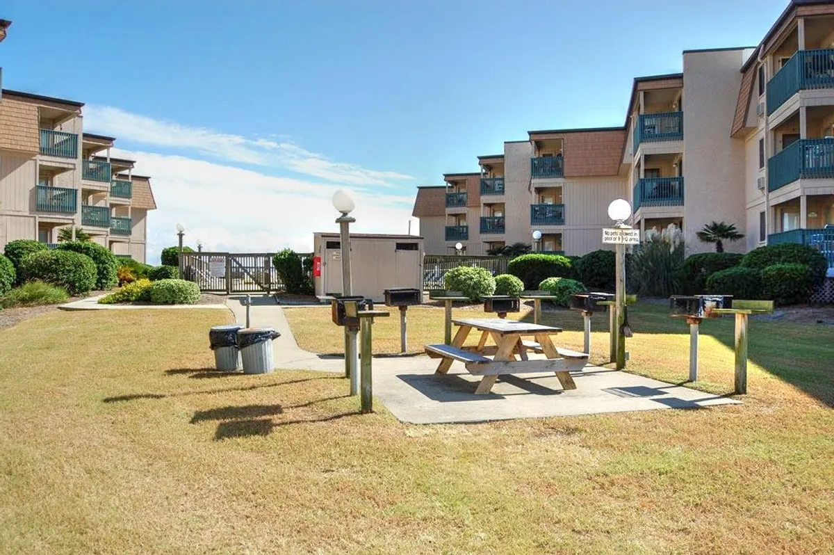 A picnic area featuring grill stations and a picnic table surrounded by lush greenery and residential facades. The setup encourages group barbecues, outdoor meals, and communal bonding under the open sky.